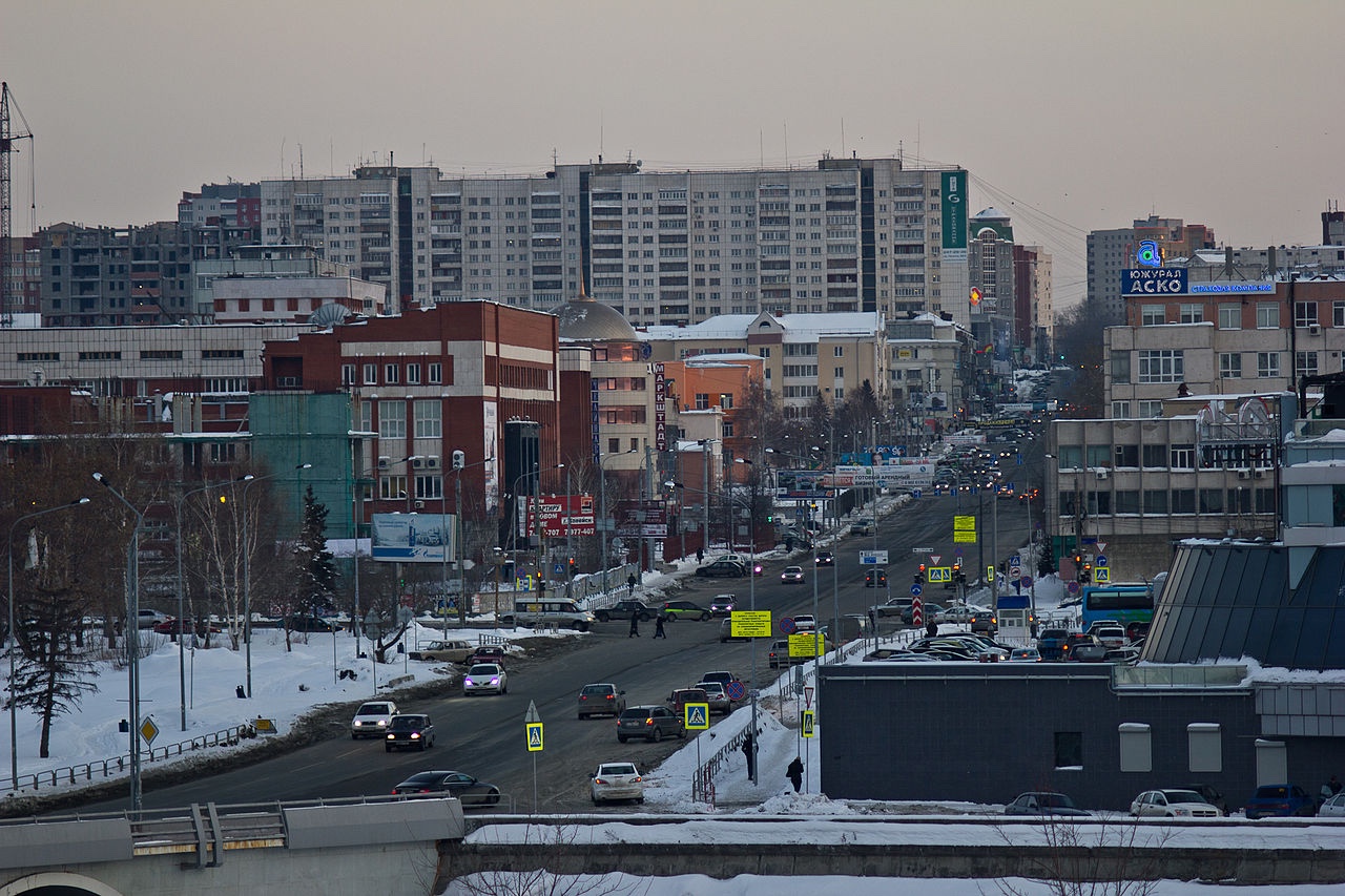 Photo of a view of a snowy city street in Chelyabinsk facing uphill with a mix of multicoloured apartment blocks, shops and other businesses